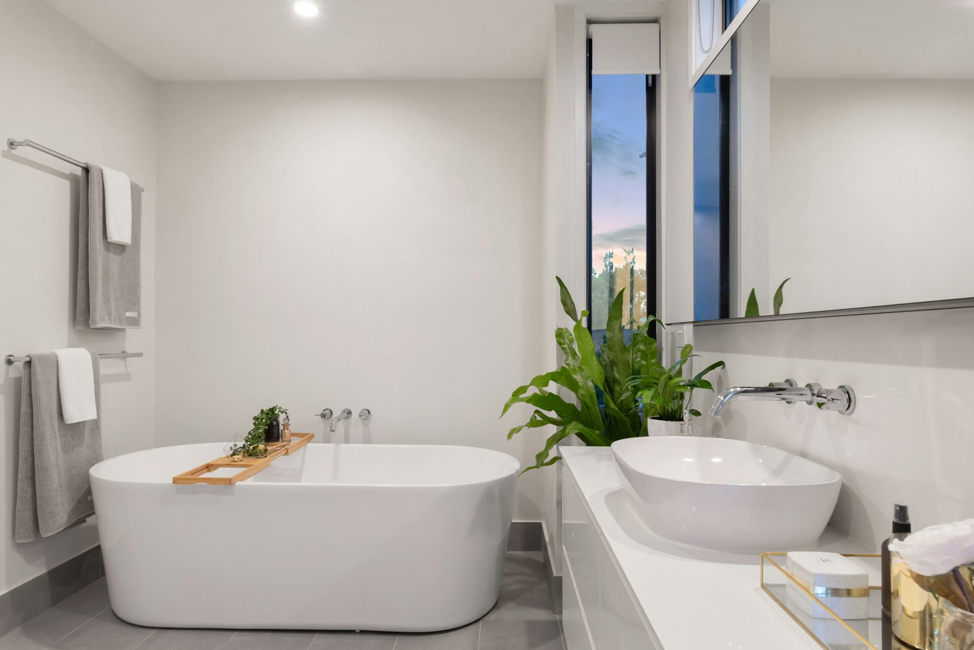 A white bathroom with a freestanding bath beside a potted plant