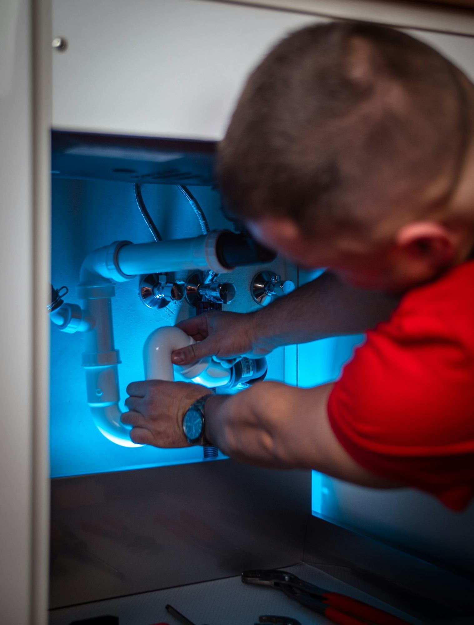 A plumber working on pipework inside a cabinet